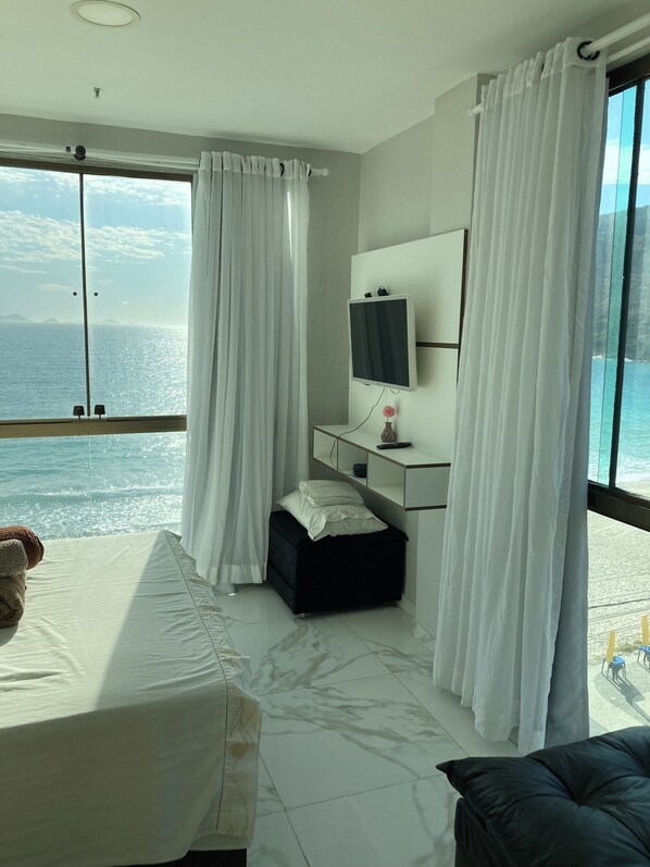 A hotel room with a bed, a bedside table, a TV, and a view of the sea.