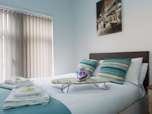 A neatly made bed with a small table, pillows, and folded towels. - Town House @ Minshull New Road (Crewe)