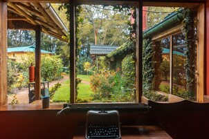 A room with a view of a garden through a large window, a wooden desk, and a typewriter.