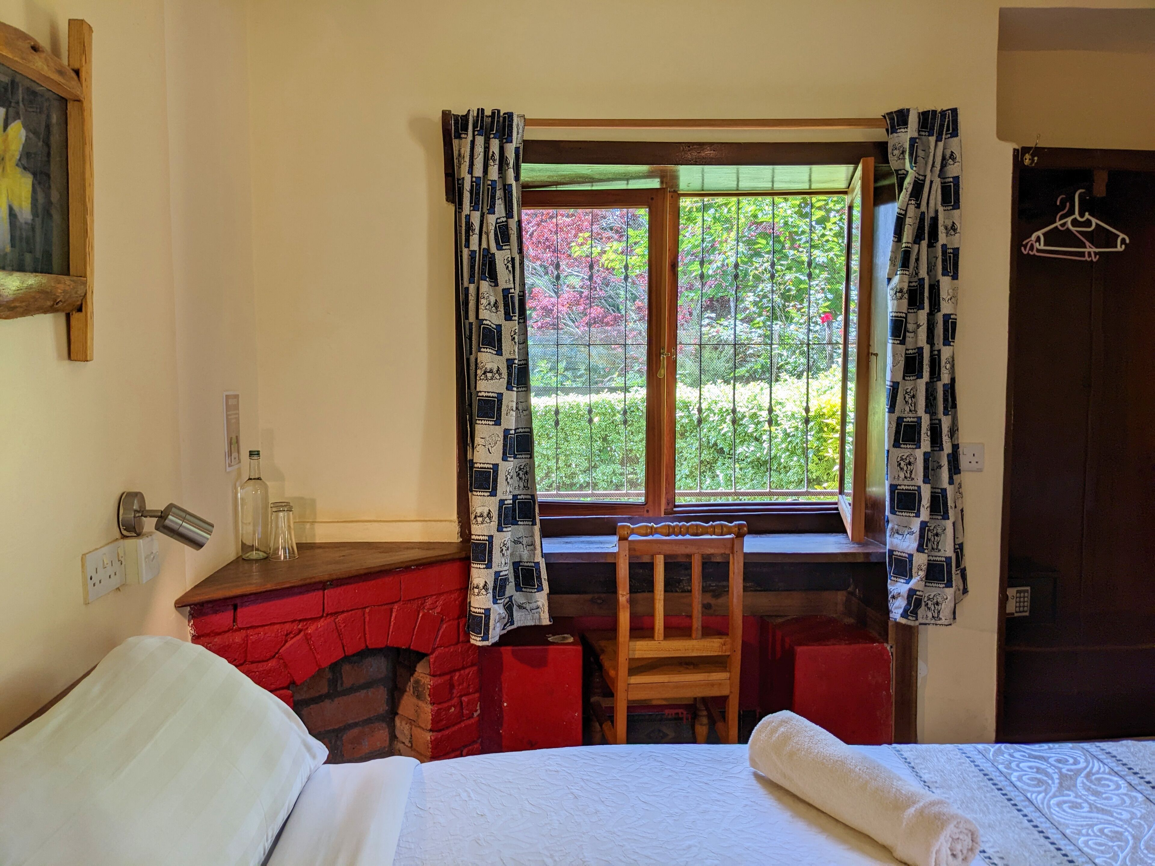 A room with a bed, a wooden chair, a fireplace, and a window with patterned curtains.