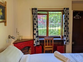 Una habitación con cama, una silla de madera, chimenea y una ventana con cortinas estampadas.