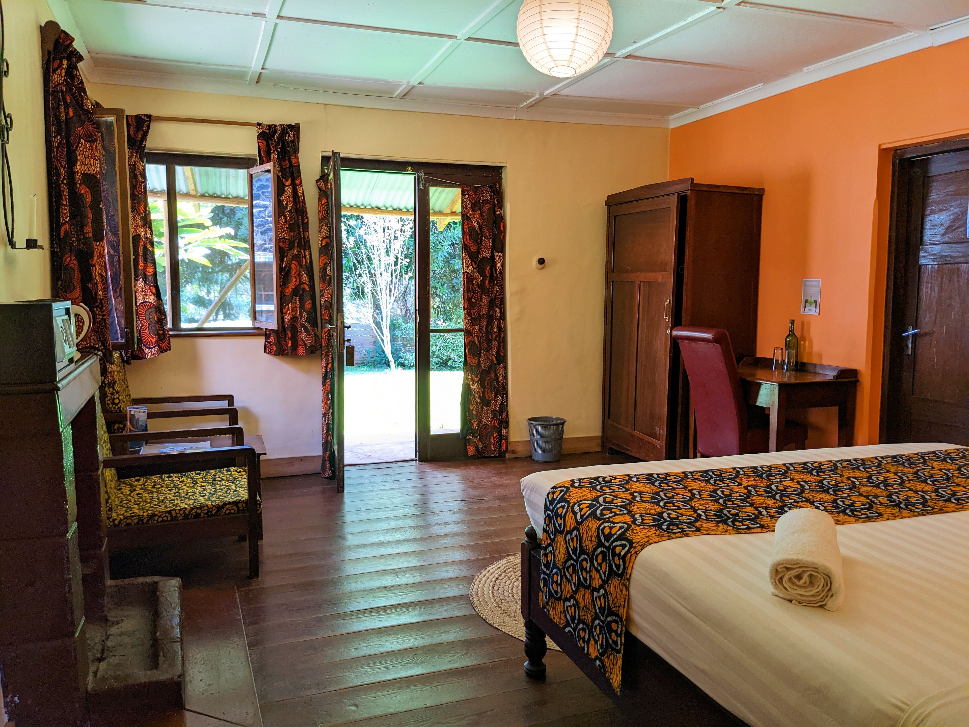 A hotel room with a bed, a desk, a wardrobe, and a view of the outdoors through a door.
