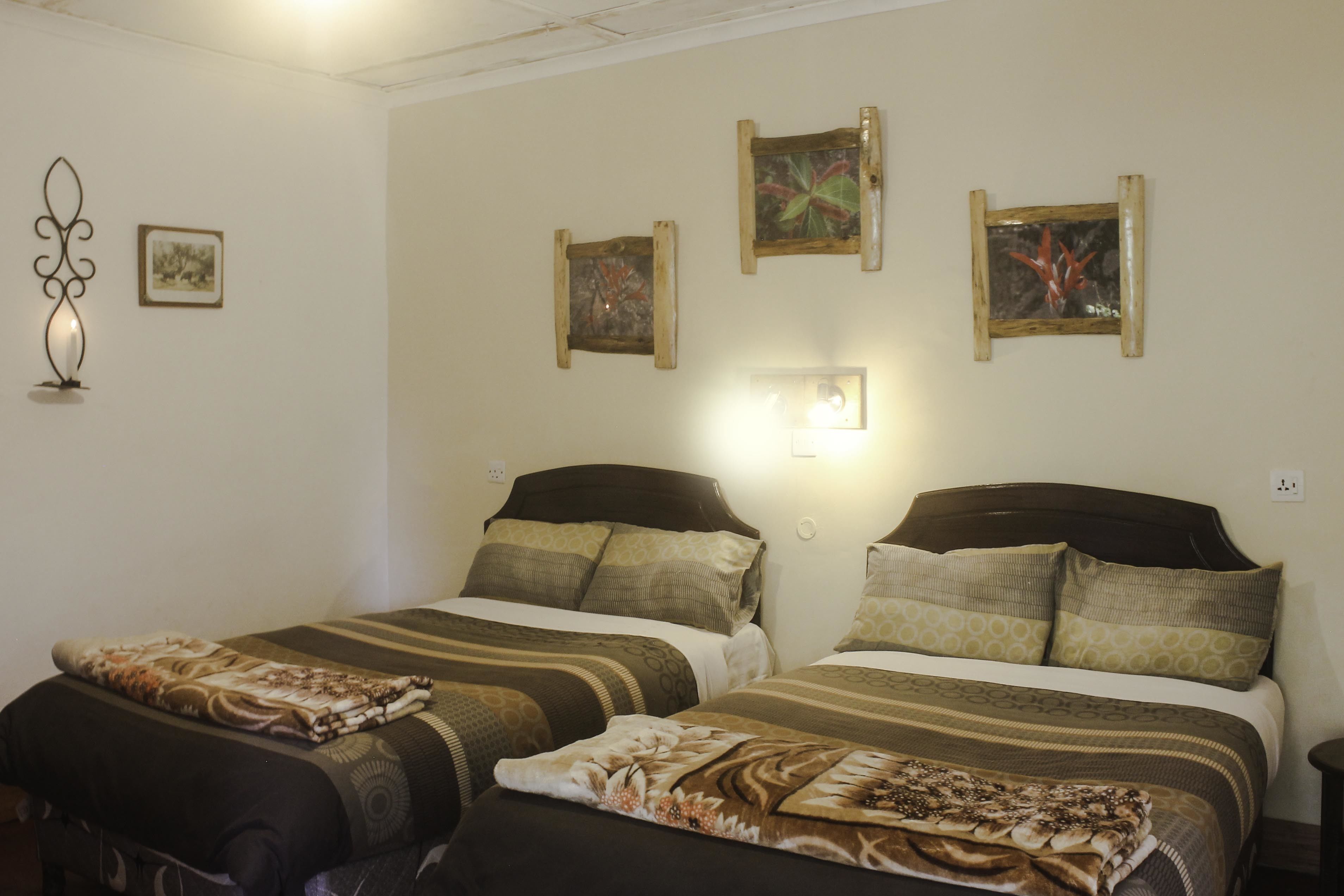 Ein Hotelzimmer mit zwei Betten, beide mit gemusterten Bettbezügen und Kissen. An der Wand hängen Bilderrahmen und eine Wandleuchte.