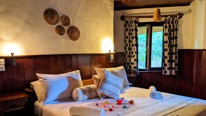 Una cama bien hecha con ropa blanca y almohadas decorativas, una mesita de noche con una lámpara y una ventana con cortinas estampadas.
