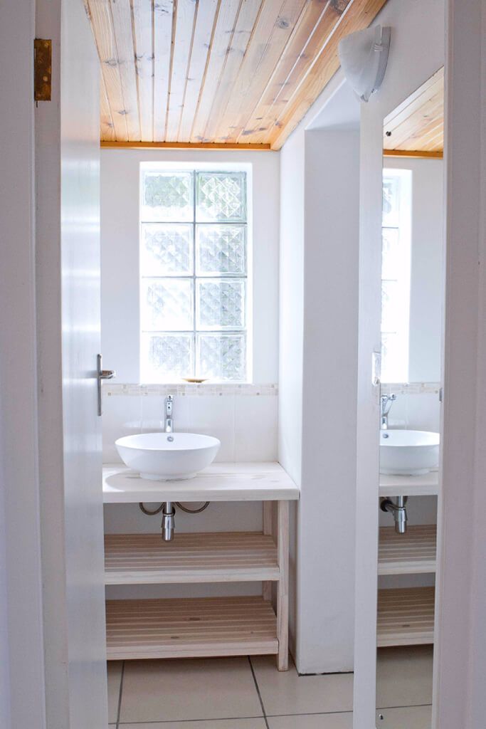 Un baño con lavamanos blanco, repisas de madera y una ventana con vidrio esmerilado.