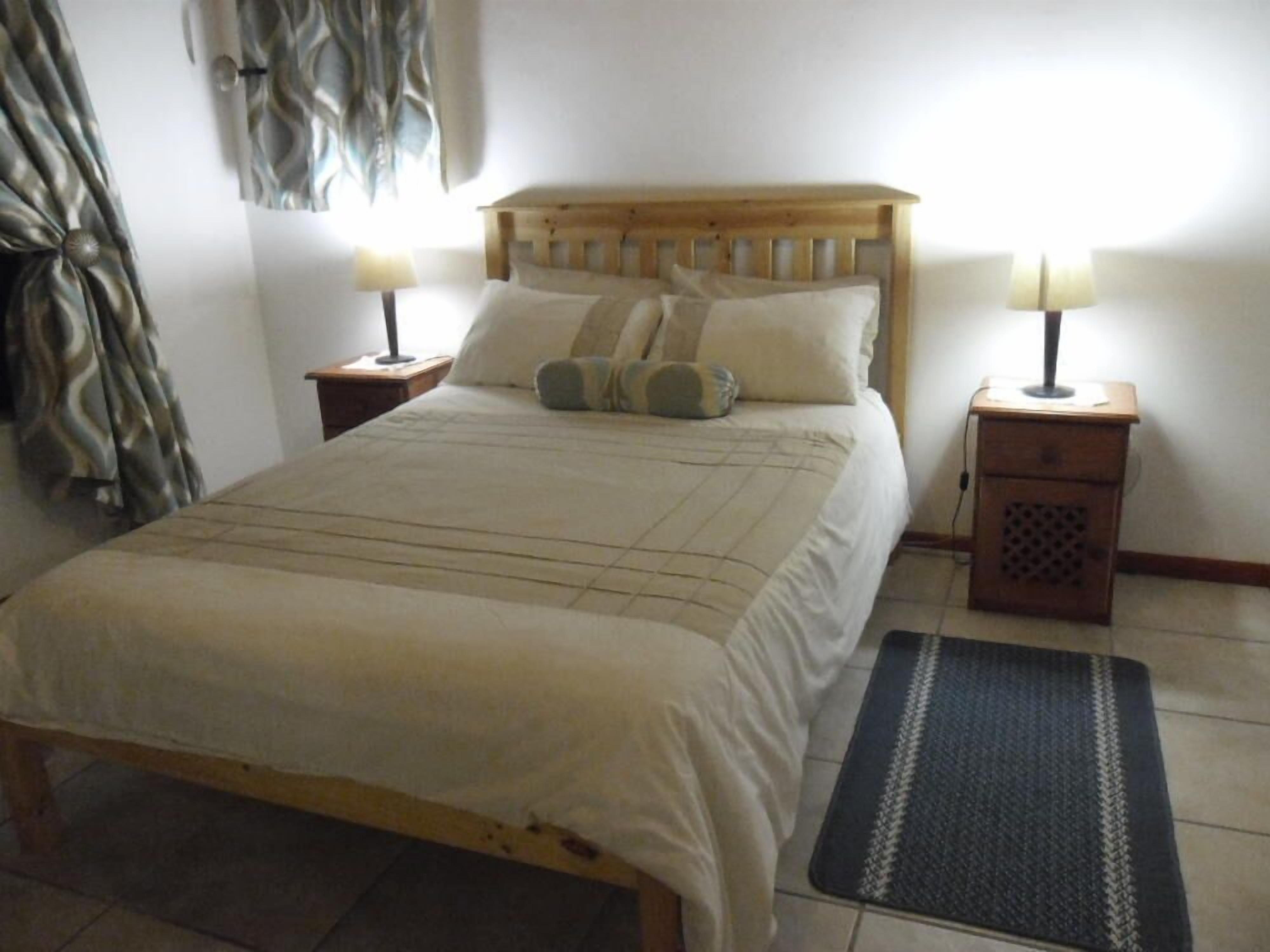 A neatly made bed with a wooden headboard, two bedside tables with lamps, and a patterned rug on the floor.