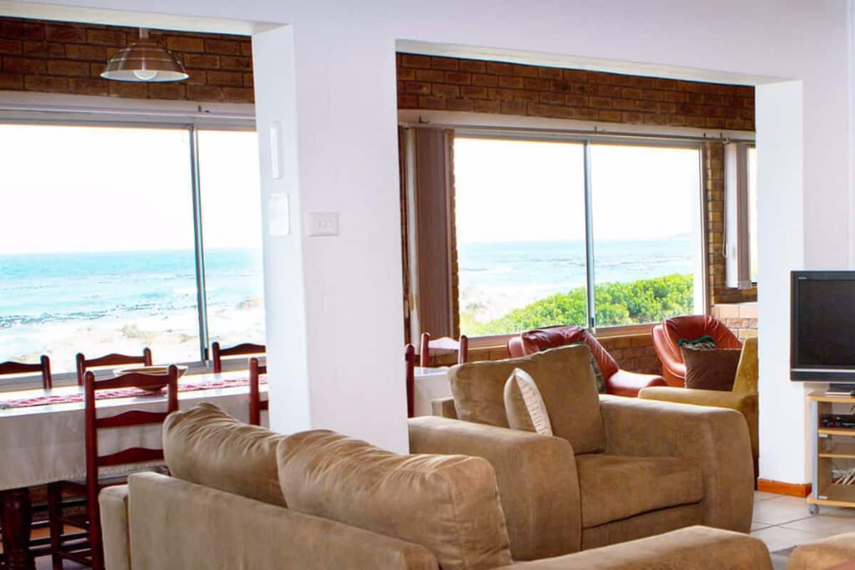 A living room with a large window overlooking the ocean, a sofa, a TV stand, and a dining area with a table and chairs.