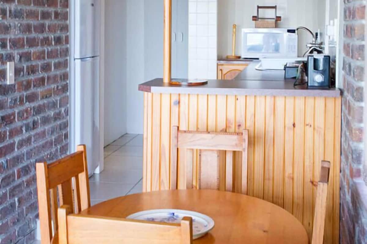 A compact kitchen with wooden cabinetry, a round dining table, and a clock on the wall.