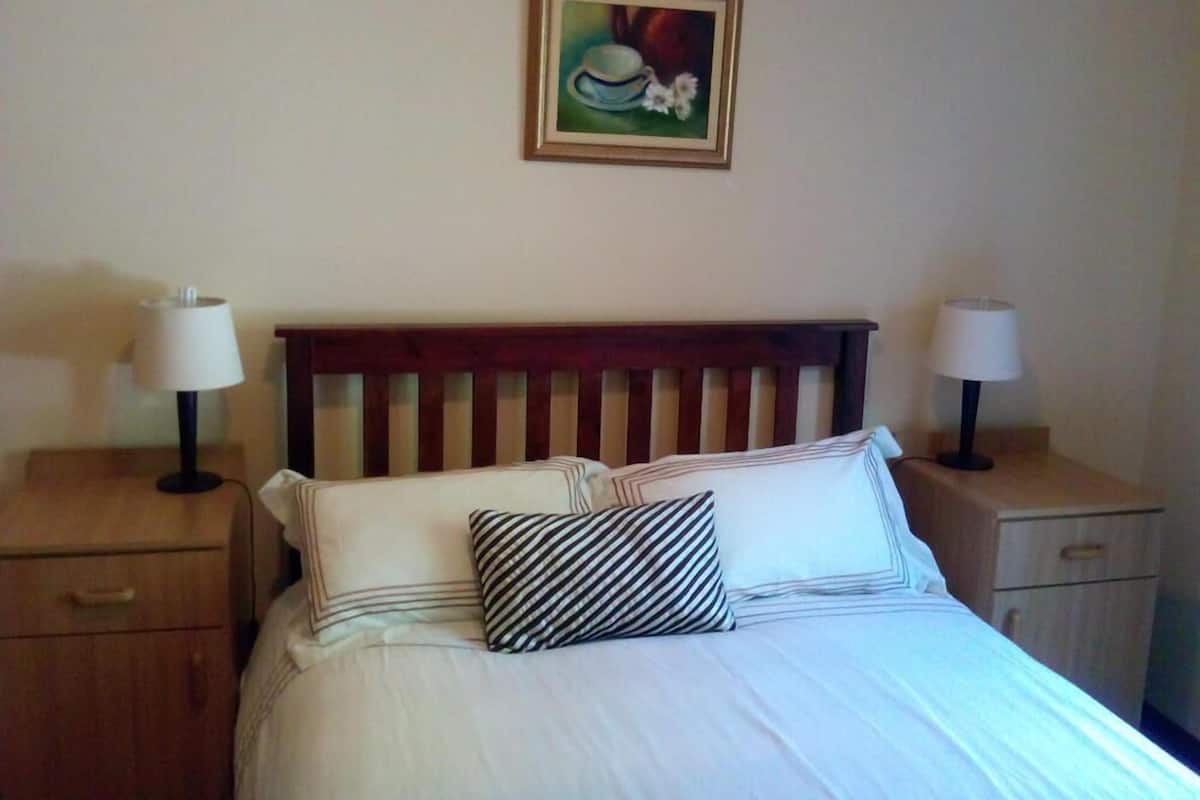 A neatly made bed with striped pillows and a wooden headboard, flanked by two bedside tables with lamps.