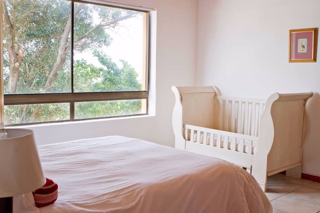 A room with a crib, a bed, a window, and a framed picture on the wall.