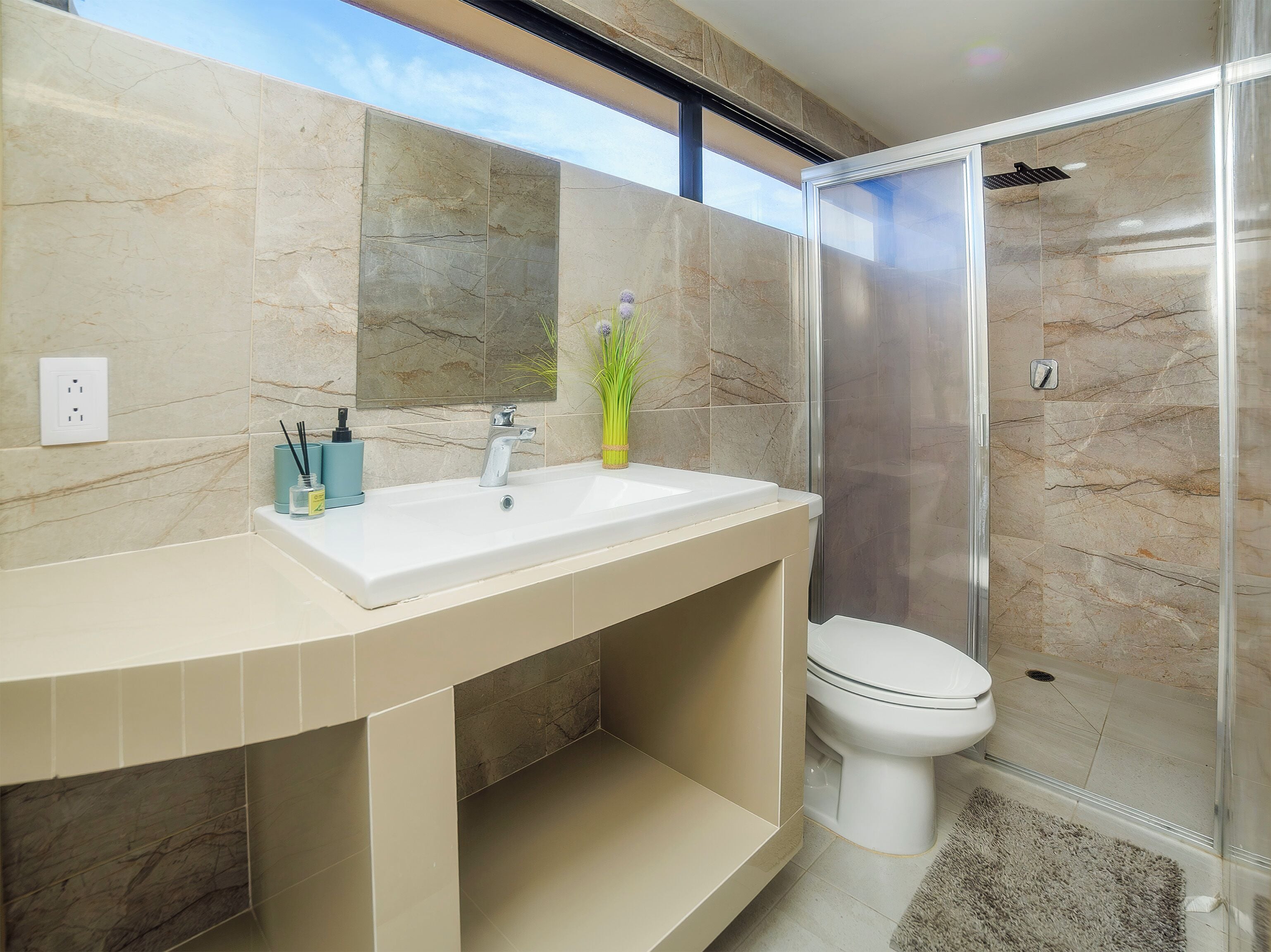 Un baño moderno con un tocador curvo, un espejo grande, un inodoro y una ducha con mampara de vidrio.