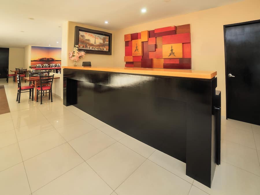 A hotel reception area with a black reception desk, a framed picture of a cityscape, and a wall with a geometric pattern.