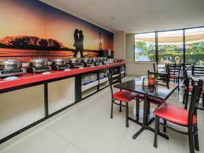 Un comedor con mesas de buffet, un mural de una pareja y vistas al exterior.