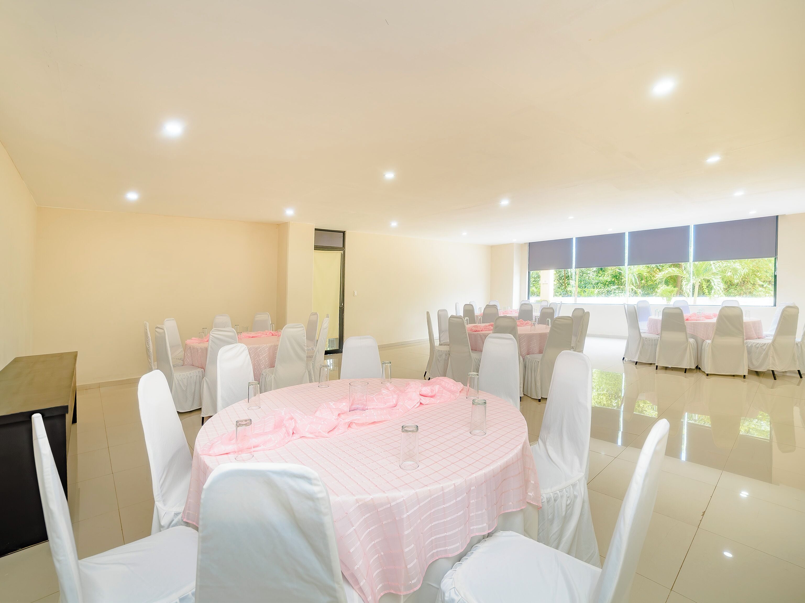Un salón de conferencias con mesas redondas, sillas blancas y un piano.