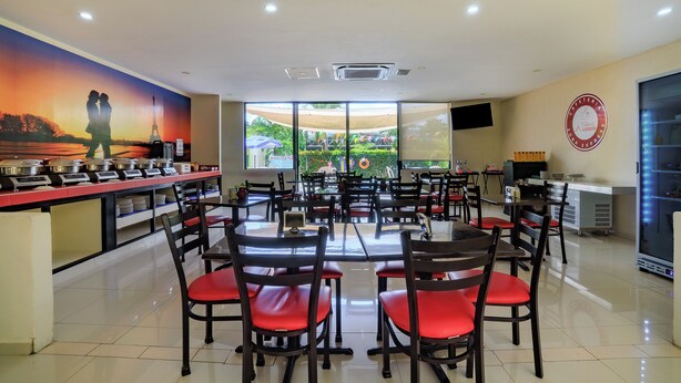 A restaurant with a buffet setup, multiple tables with chairs, and a large window offering a view of greenery.