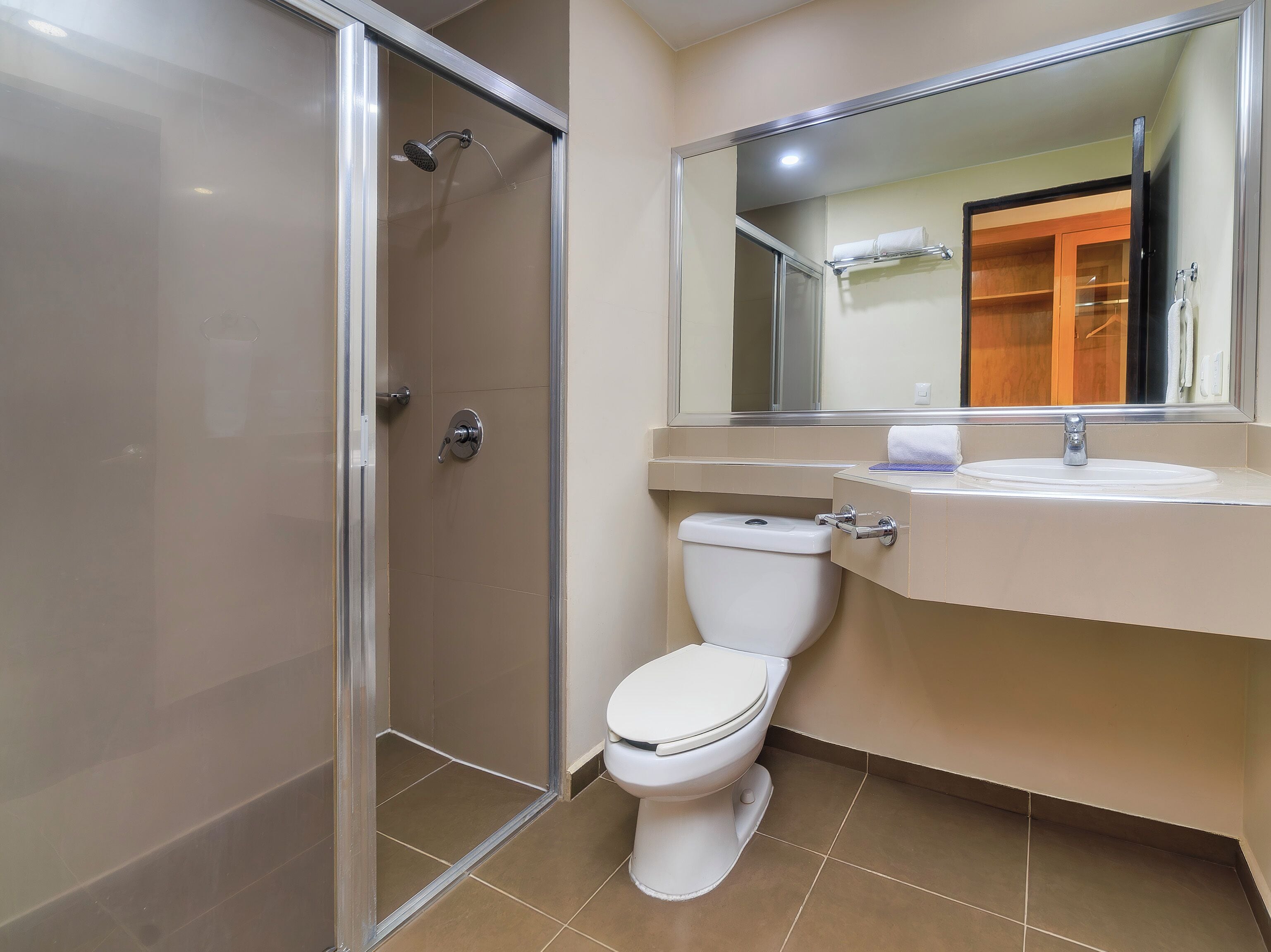 A bathroom with a shower, toilet, sink, and mirror.