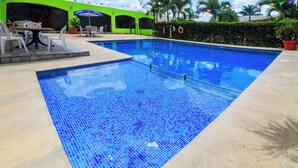 A swimming pool with a tiled edge, surrounded by a patio area with chairs and tables.
