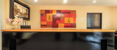 A reception desk with a black counter, a framed picture of a cityscape, a colorful abstract wall art, and a vase with flowers.