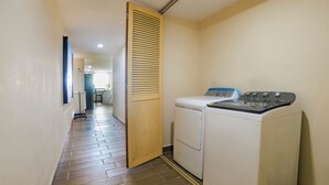 A laundry room with a washing machine and dryer, wooden door, tiled floor, and a hallway leading to a room with a bed and window. - Collection O Paris FC Express, Poza Rica de Hidalgo (Poza Rica)