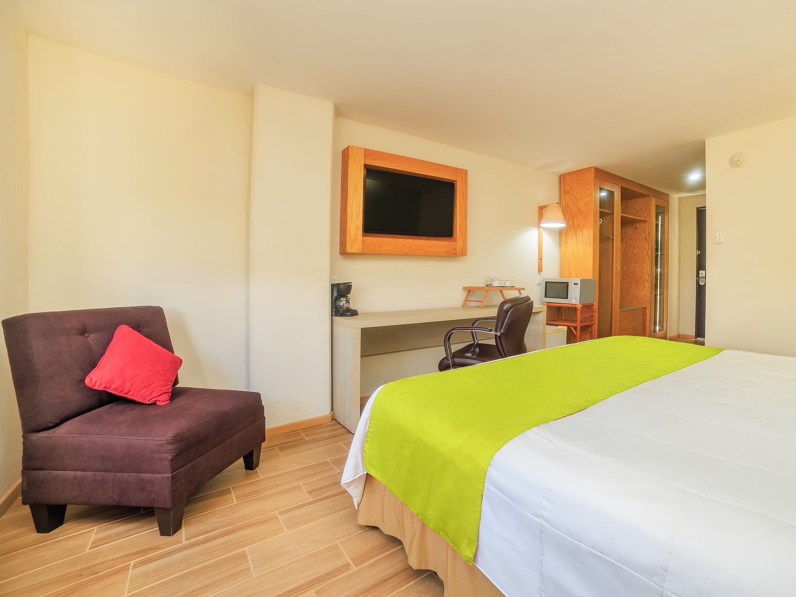 A hotel room with a bed, a desk, a chair, a television, and a wardrobe.