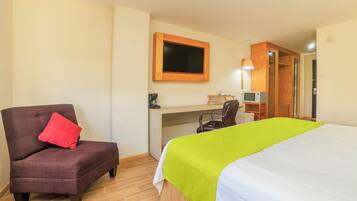 A hotel room with a bed, a desk, a chair, a television, and a wardrobe.