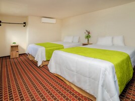 Habitación de hotel con dos camas, una mesita de noche pequeña, aire acondicionado de pared y alfombra estampada.