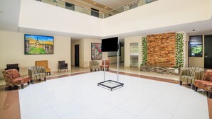 A spacious lobby with a high ceiling, a central seating area with chairs, a flat-screen TV mounted on the wall, and a decorative wall with a brick pattern. - Collection O Paris FC Express, Poza Rica de Hidalgo (Poza Rica)