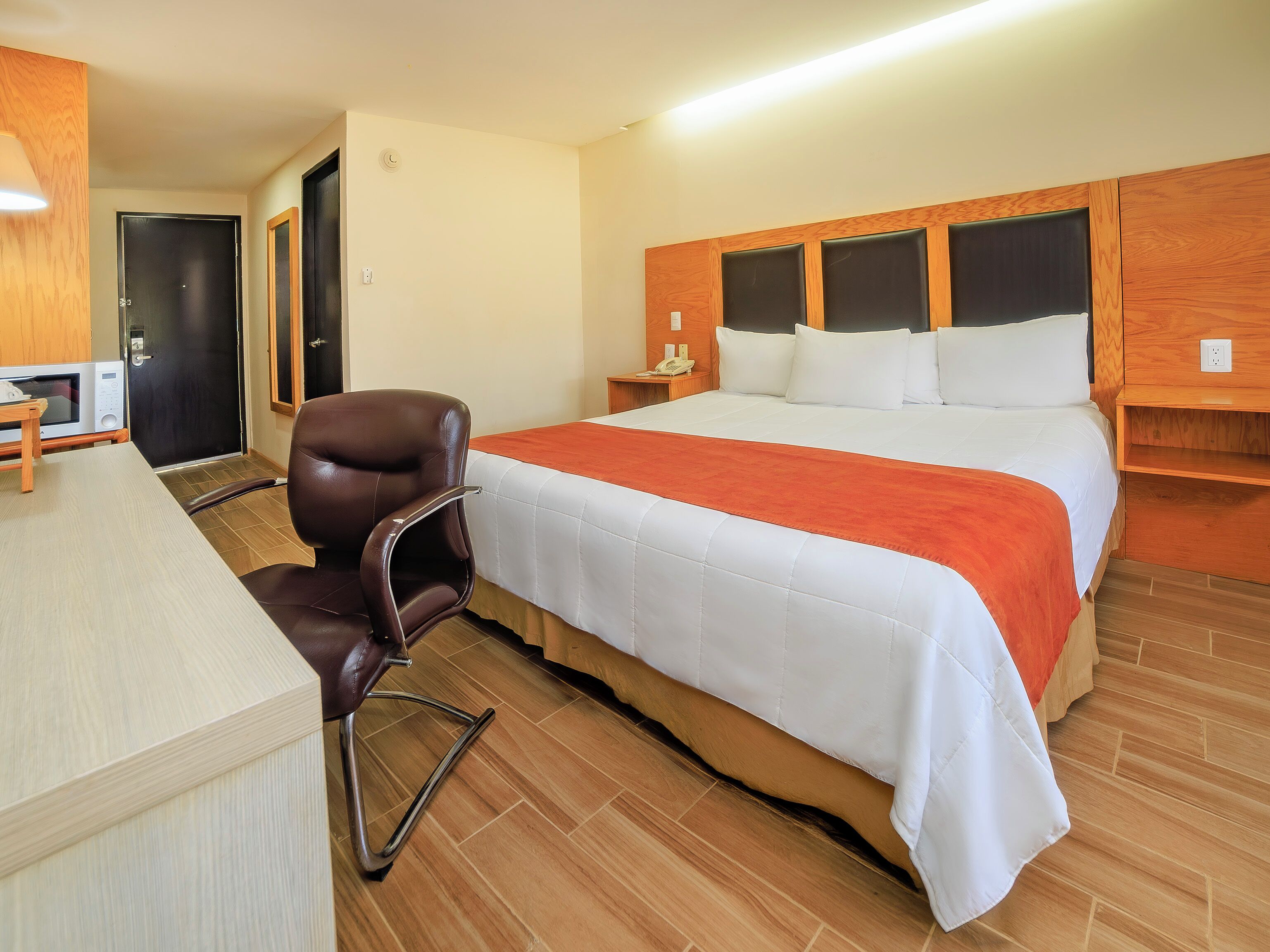 A hotel room with a bed, a desk, a chair, a microwave, and a door.