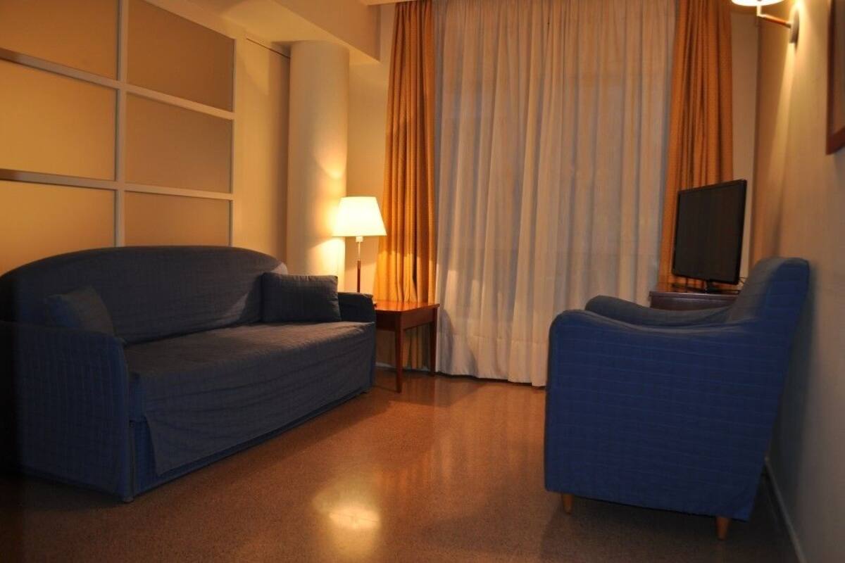 Une chambre d’hôtel avec un canapé, un fauteuil, une lampe et un téléviseur.