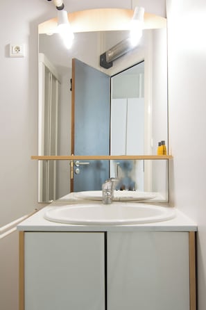A bathroom with a white sink, a mirror, and a door. - Résidence Carpe Diem (Marseille)