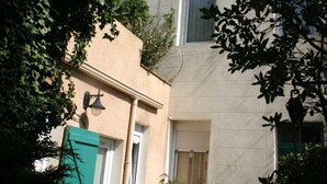 A narrow alleyway with a building featuring a light-colored facade, a green door, and a small table with a potted plant. - Résidence Carpe Diem (Marseille)