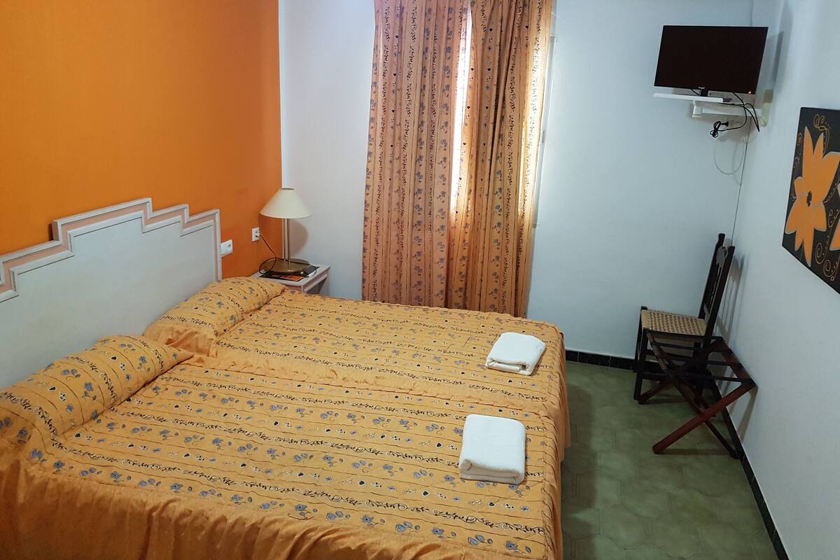 Quarto de hotel com cama, cadeira, televisão e ar condicionado.