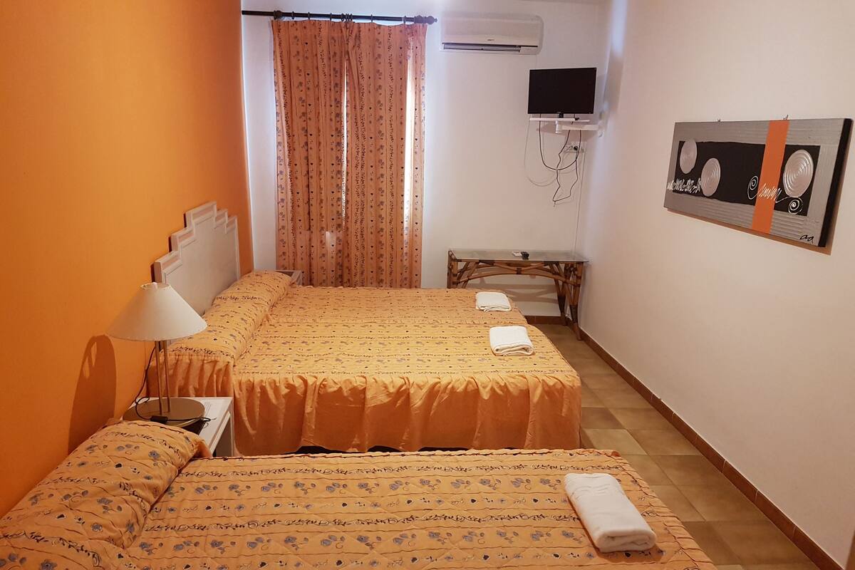 Quarto de hotel com duas camas, uma escrivaninha, uma TV e um ar condicionado.