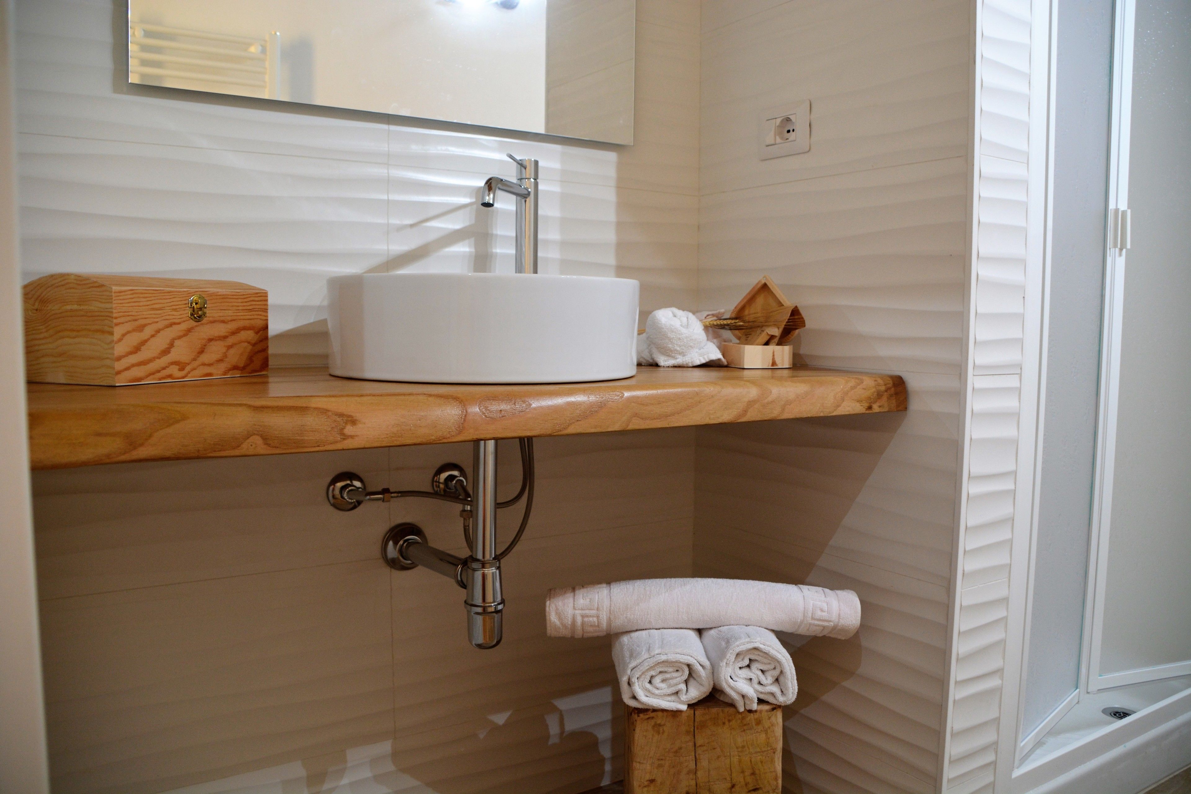 Une salle de bain avec un meuble-lavabo en bois, un lavabo blanc et un miroir au-dessus. On y trouve un porte-serviettes avec des serviettes et une boîte en bois posée sur le meuble-lavabo.