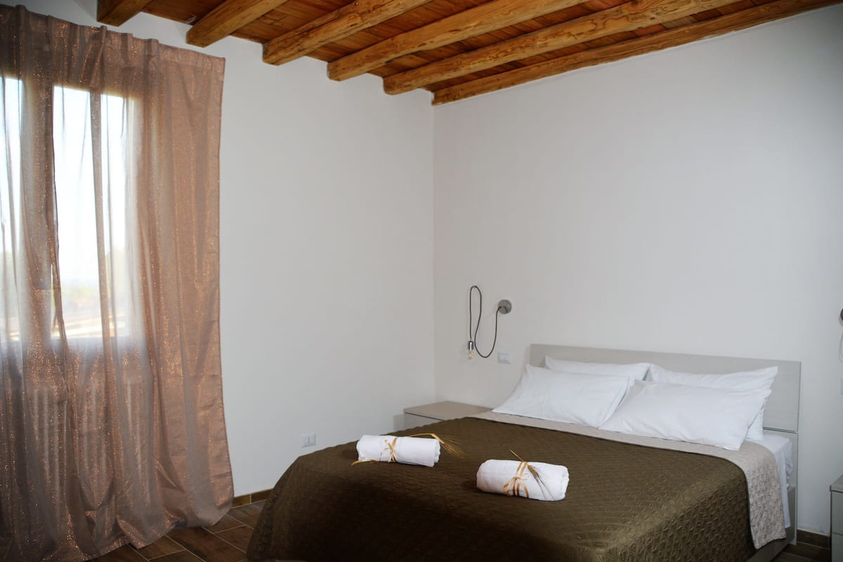 Une chambre avec un plafond en bois, un lit recouvert de draps blancs, une couverture marron et une salle de bain avec douche.