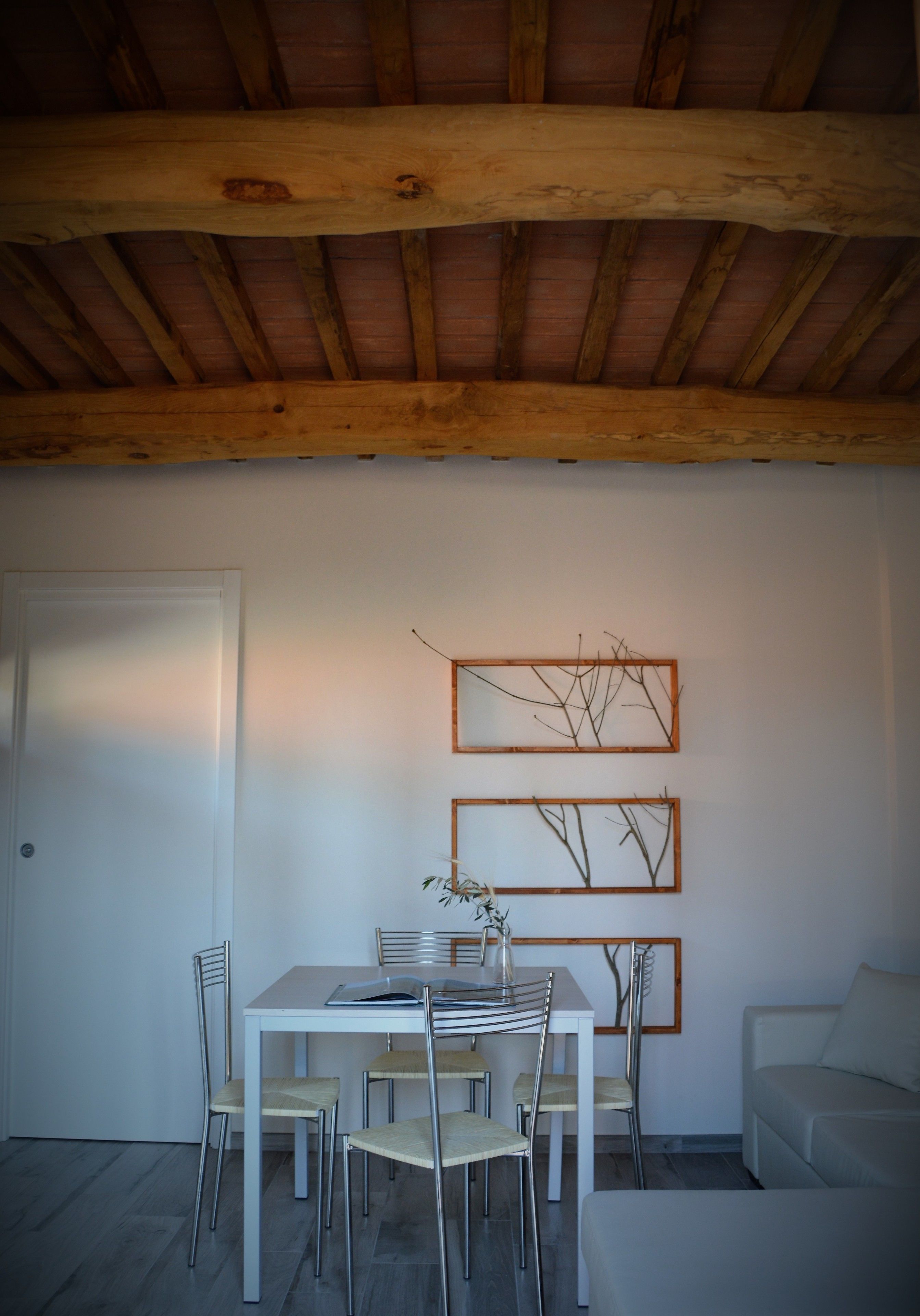 A dining area with a white table and chairs, a wooden ceiling, and wall-mounted branch art.