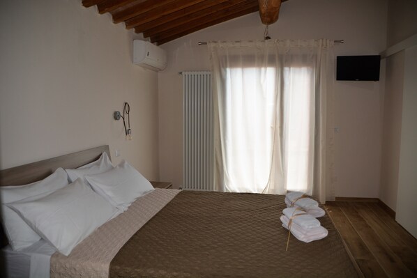 A bedroom with a bed, a wooden headboard, a window with curtains, a wall-mounted TV, and a radiator. - Agriturismo L'Aquilone (Magliano in Toscana)