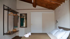 Een slaapkamer met een bed, houten plafond, een garderobe, een spiegel en een plank met schoenen en een handtas.
