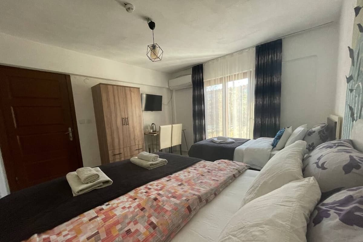 A hotel room with a bed, a desk, a chair, a wardrobe, and a window with curtains.