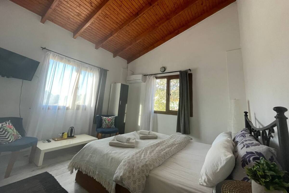 A bedroom with a wooden ceiling, a bed with pillows and towels, a chair, a bedside table, and a window with curtains.