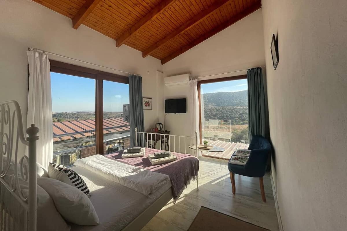 A bedroom with a large bed, a TV, and a balcony with a view of the countryside.