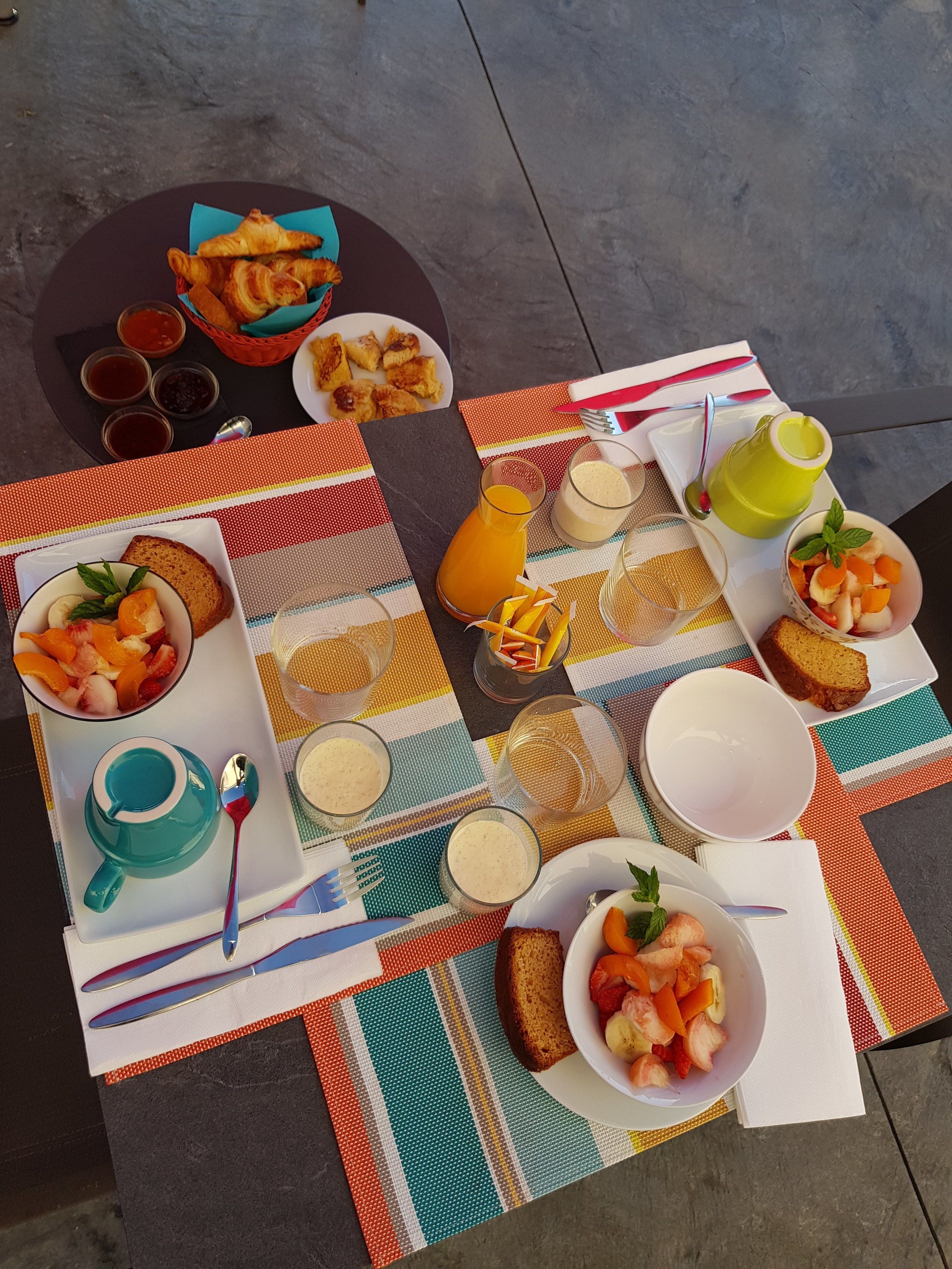 Una mesa dispuesta con artículos para el desayuno, incluyendo cruasanes, fruta y bebidas.