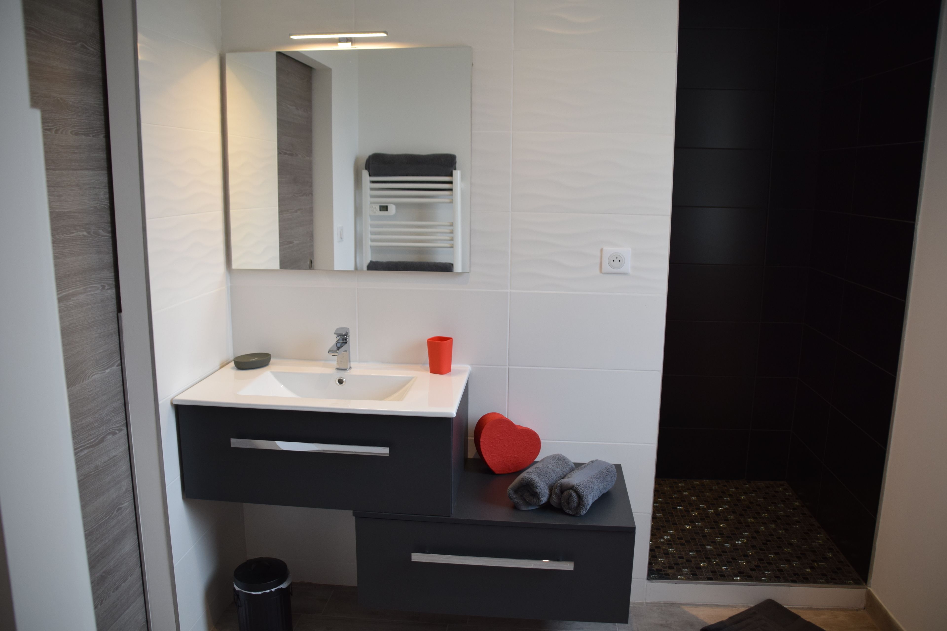 Un baño moderno con un lavamanos blanco, tocador negro y un objeto con forma de corazón rojo sobre la encimera.