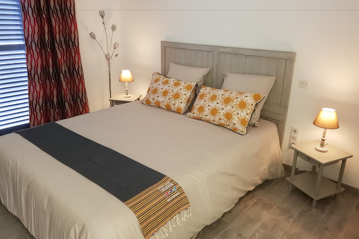 A neatly made bed with a patterned throw, two bedside lamps, and a decorative vase on a nightstand.