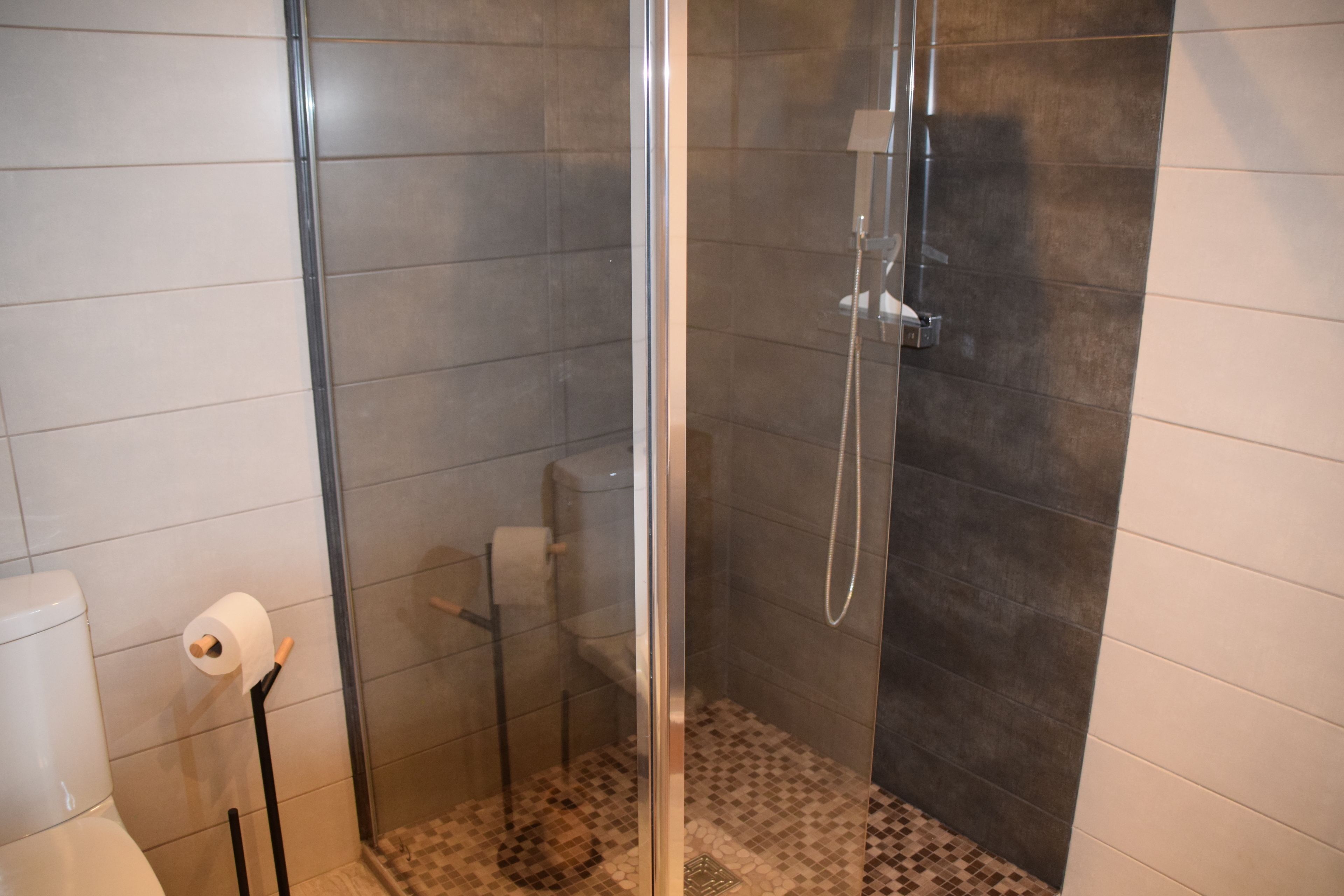 Um chuveiro com portas de vidro, um vaso sanitário e um rolo de papel higiênico em um suporte.