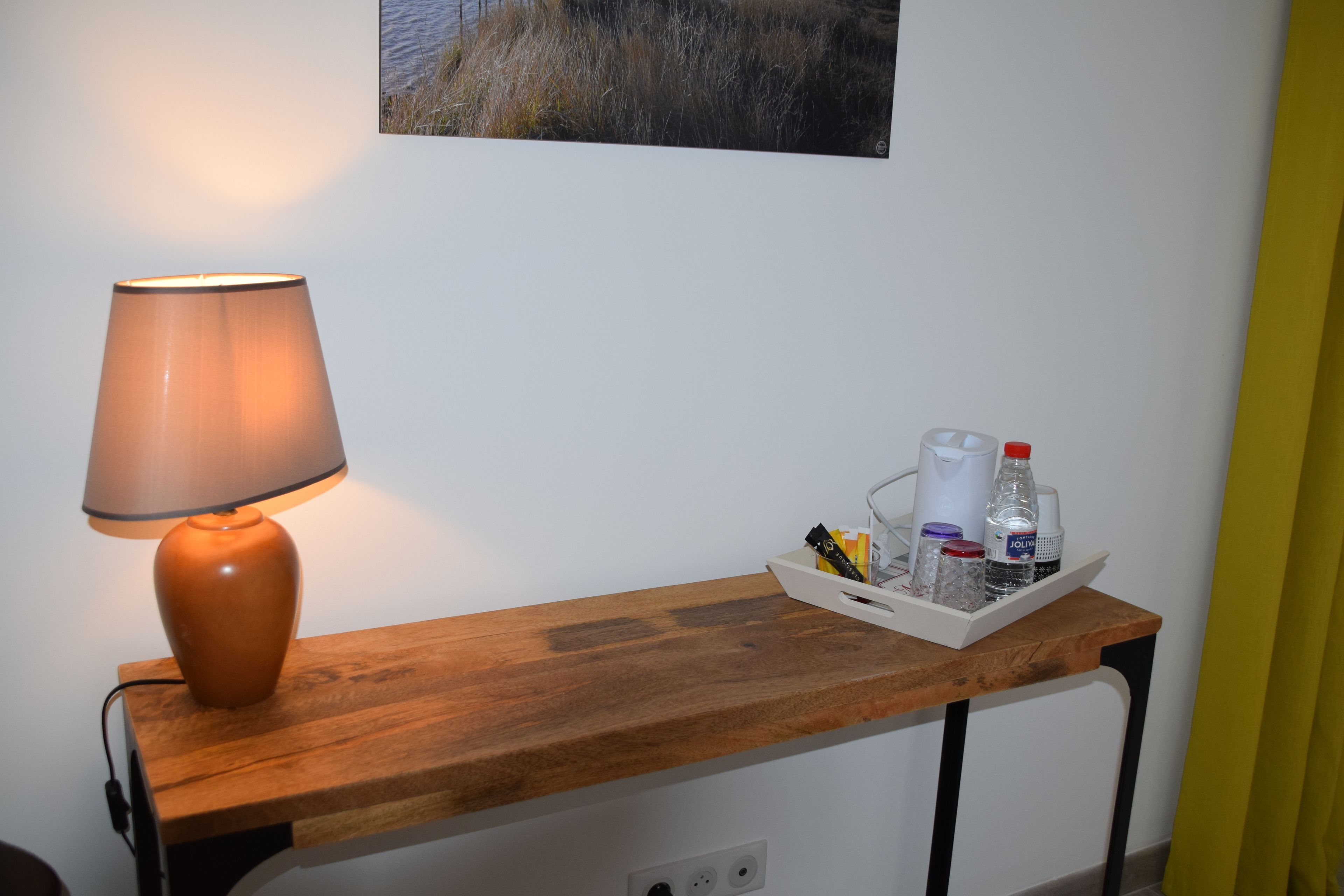 Een houten tafel met een lamp en een dienblad met flessen en glazen.