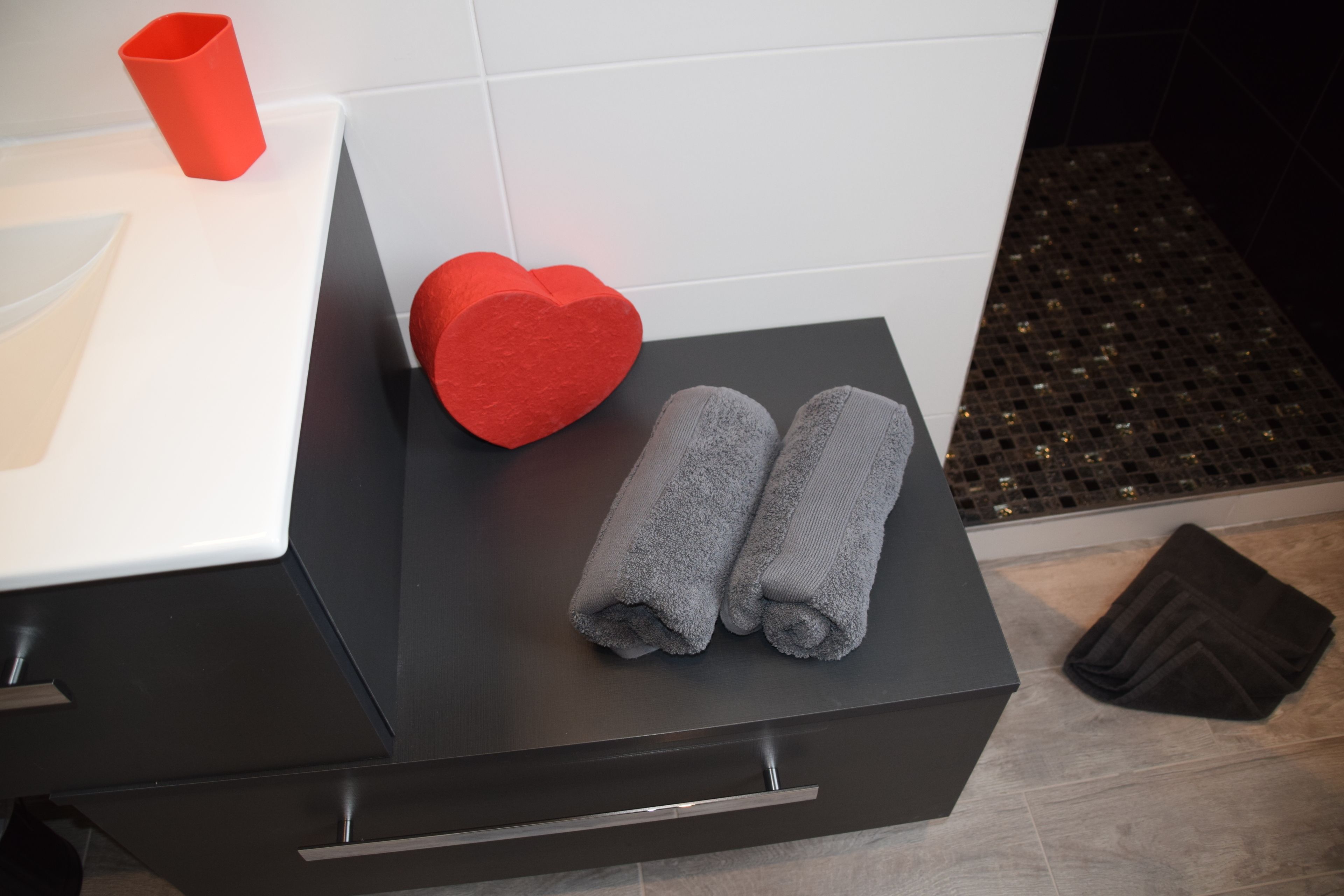 A bathroom with a black countertop, a red heart-shaped object, and two rolled towels.