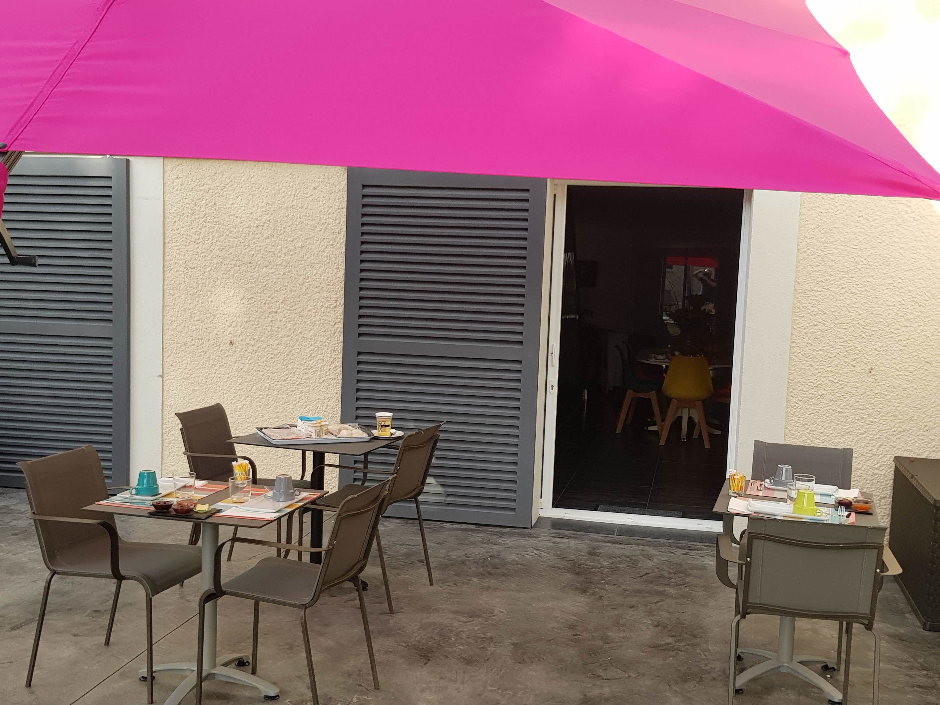 An outdoor patio area with a table and chairs, a pink umbrella, and a sliding door leading to an interior space.