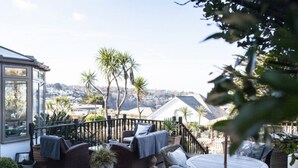A patio with wicker furniture, a glass enclosure, and a view of a residential area with palm trees. - Headland House Luxury B&B (St Ives)
