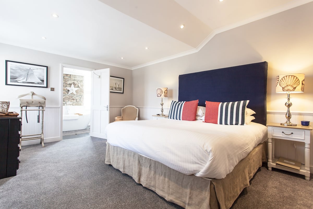 Een keurig opgemaakt slaapkamer met een groot bed, nachtkastjes en een deur naar een badkamer.